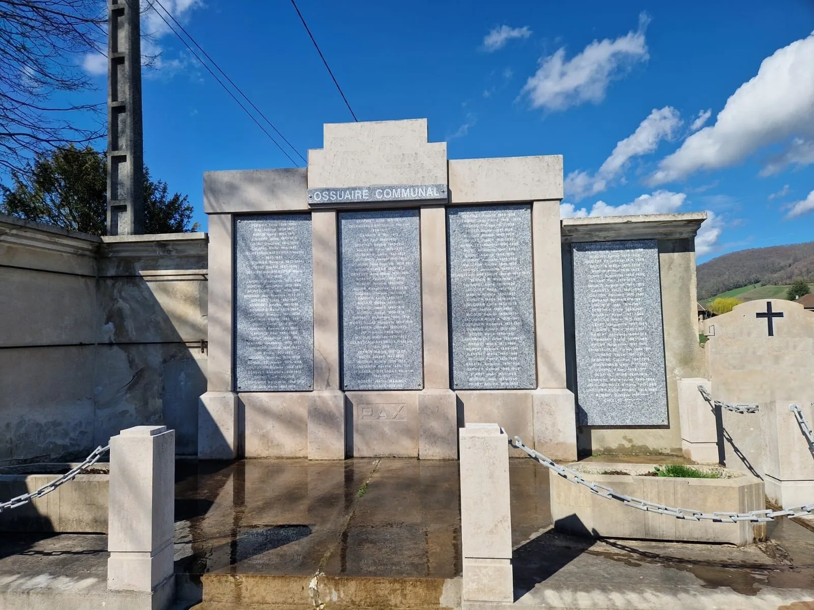 Ossuaire communal avec plaques commémoratives en marbre gravées de noms sous un ciel bleu
