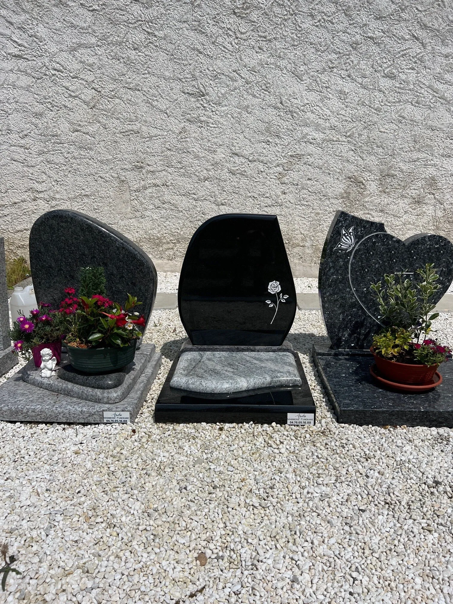 Trois monuments funéraires modernes en granit noir et gris avec gravures et compositions florales