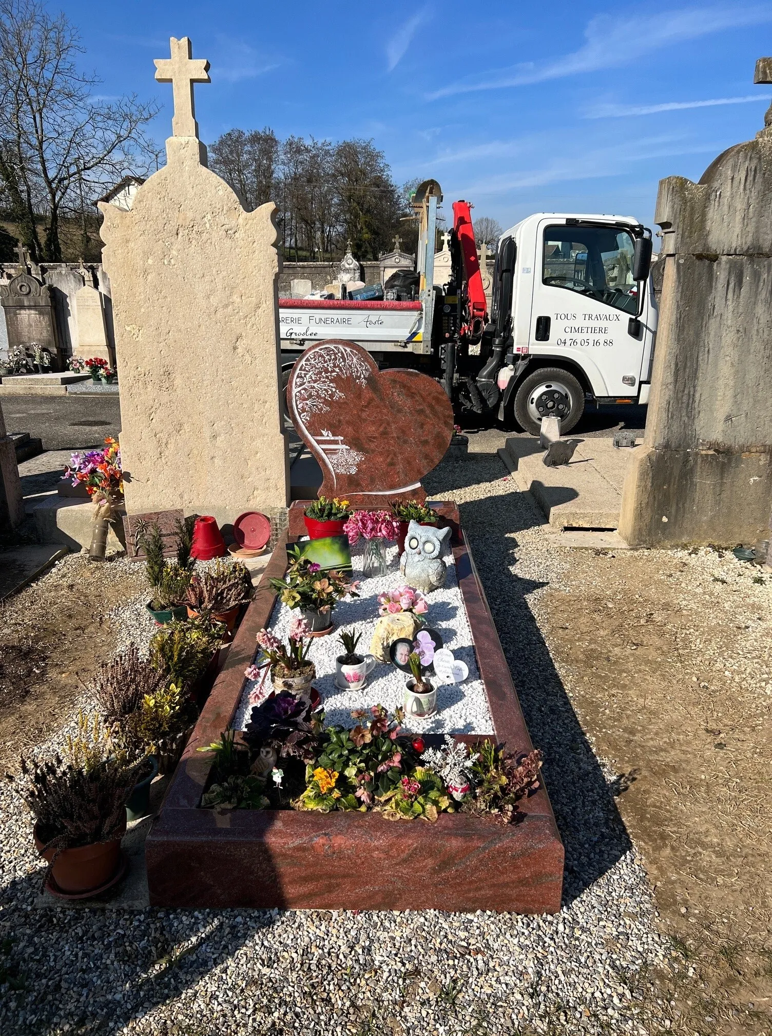 Tombe avec stèle en forme de cœur en granit rouge, ornée de fleurs et de plaques