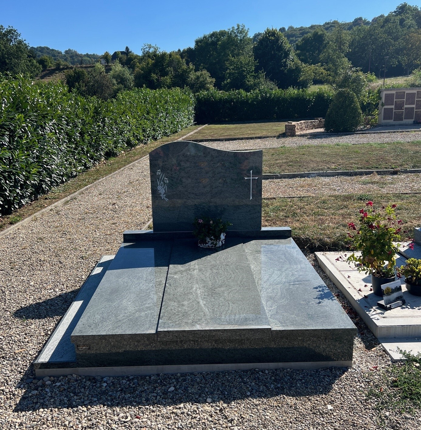 Grand monument funéraire en granit gris foncé et poli dans un cimetière verdoyant